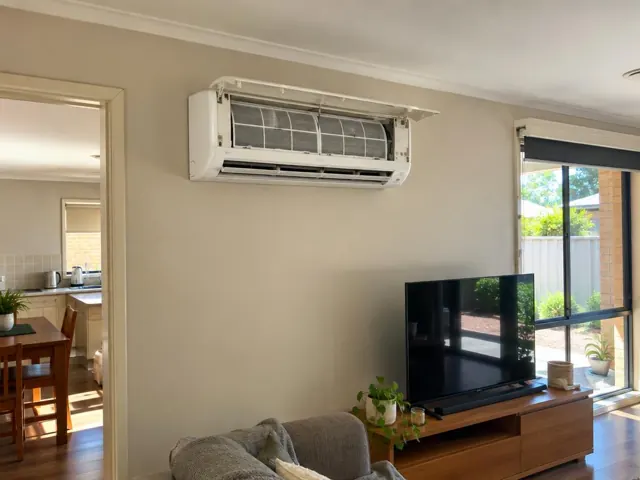 Open split-system air conditioner with filters visible above a living room TV in a beige home in Blakeview