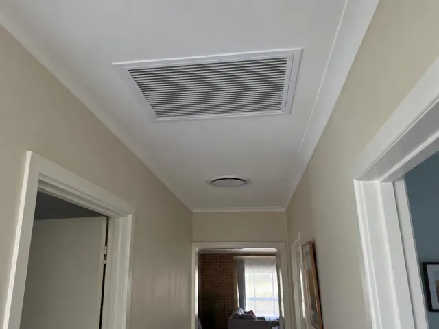 Hallway ceiling with a return-air grille and round ceiling outlet above cream walls in Munno Para